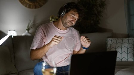 Ein junger hispanischer Mann genießt zu Hause Musik über Kopfhörer und zeigt Entspannung, Unterhaltung und Lebensstil.