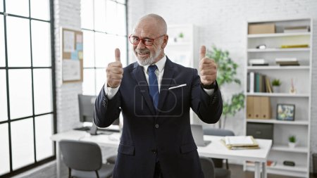 Professionnel senior homme avec barbe en costume donnant pouces vers le haut dans le bureau moderne