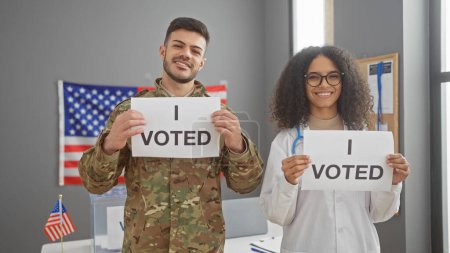 Un hombre con uniforme militar y una doctora sosteniendo letreros de "yo voté" frente a una bandera de nosotros en el interior