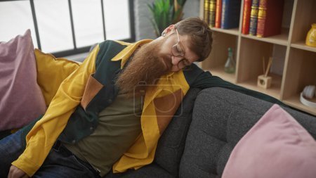 Rotschopf bärtiger Mann schläft auf einem Sofa mit bunten Kissen in einem gemütlichen Innenraum