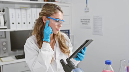 Photo for Serious and beautiful blonde woman scientist, deep in thought at lab, young pro working on touchpad amidst test tubes, focused on medical research - Royalty Free Image