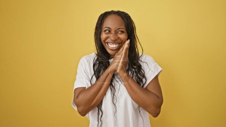 Smiling young african american woman with curly hair against a yellow isolated background, radiating happiness and positivity.