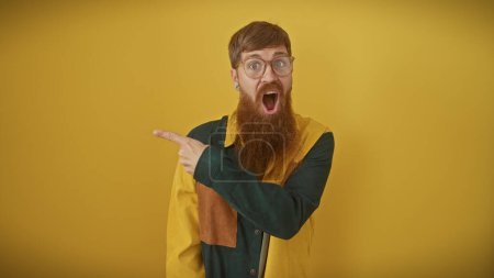 Photo for Excited redhead man with beard pointing left against yellow background - Royalty Free Image