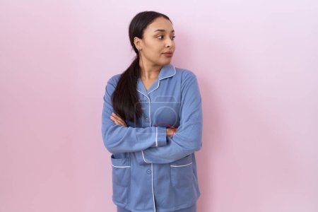 Téléchargez les photos : Jeune femme arabe portant un pyjama bleu regardant sur le côté avec les bras croisés convaincus et confiants - en image libre de droit