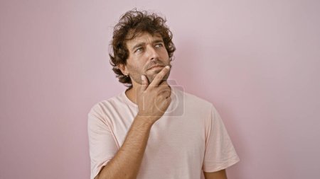 Photo for Pensive young hispanic man in casual attire contemplating against a plain pink wall. - Royalty Free Image