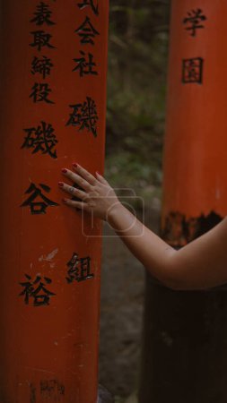 Paseo reverente de la joven mujer, caminando y tocando las puertas torii japonesas tradicionales en fushimi inari-taisha, una mirada hacia atrás mientras se mueve a lo largo del camino naranja de madera