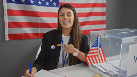 Mujer hispana sonriente con etiqueta 'voté' apuntándose a nosotros centro de interior del colegio electoral con bandera americana.