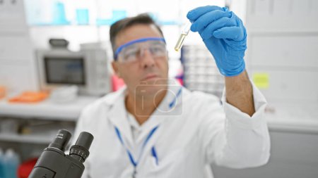 A mature man in a white lab coat analyzing a test tube with a serious expression in a laboratory setting.