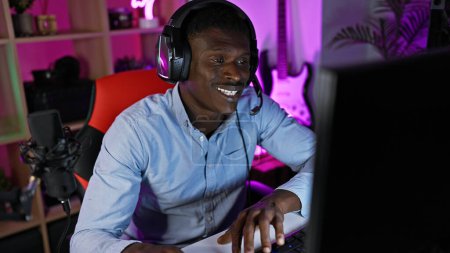 Photo for An african american man engaged in gaming with headphones in a colorful illuminated room at night. - Royalty Free Image