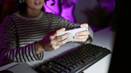 Photo for A young hispanic woman enjoys mobile gaming in a dark room lit by the colorful glow of an rgb keyboard. - Royalty Free Image