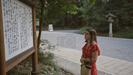 Radiant hispanic woman engrossed in reading meiji temple map and history, captivating beauty enhanced by glasses, thriving in japan's vibrant culture and timeless landmarks