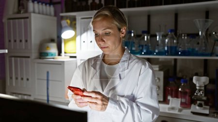 Téléchargez les photos : Une jeune scientifique en blouse blanche utilise un smartphone dans un cadre de laboratoire moderne. - en image libre de droit