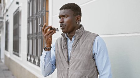 Schöner schwarzer Mann benutzt Diktiergerät auf Smartphone in der städtischen Straße