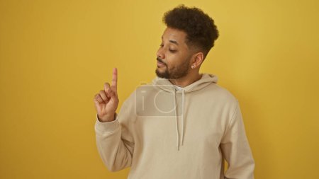 Téléchargez les photos : Portrait d'un homme afro-américain confiant geste numéro un isolé sur un fond jaune. - en image libre de droit