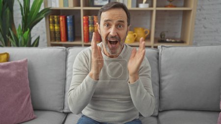 A surprised middle-aged man with a beard sitting on a sofa in a cozy living room expressing excitement