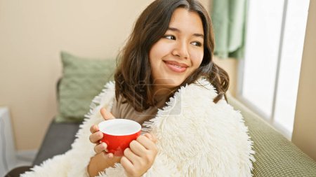 Foto de A cheerful young hispanic woman enjoys a cozy moment with coffee at home, radiating beauty and comfort. - Imagen libre de derechos