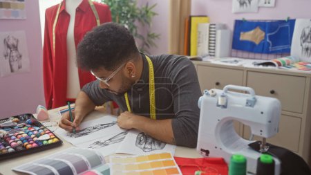 Téléchargez les photos : Homme africain tailleur avec crayon et des échantillons de tissu dans un atelier lumineux - en image libre de droit