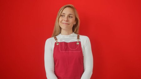 Téléchargez les photos : Femme blonde souriante en haut blanc et salopettes rouges sur un fond rouge uni - en image libre de droit