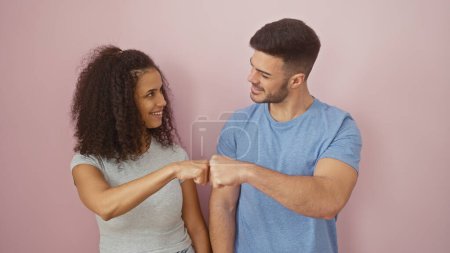 A joyful woman and man fist-bumping against a plain pink background, depicting a positive relationship.
