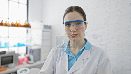 Foto de Mujer científica caucásica en laboratorio con gafas de seguridad y bata de laboratorio mirando a la cámara - Imagen libre de derechos