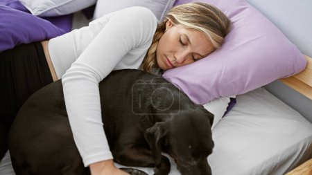 Foto de Una joven mujer caucásica abraza cariñosamente a su labrador negro dormido en un ambiente acogedor dormitorio, ilustrando un momento pacífico y cariñoso. - Imagen libre de derechos