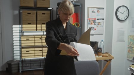 A professional woman reviews documents in a cluttered police department office, indicating a likely crime investigation.