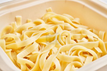 Großaufnahme frischer, ungekochter Fettuccine-Pasta in einem Plastikbehälter, der die italienische Küche hervorhebt.