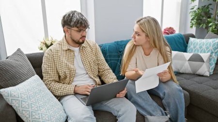 Eine Frau und ein Mann begutachten gemeinsam Dokumente in einem modernen Wohnzimmer mit Laptop.