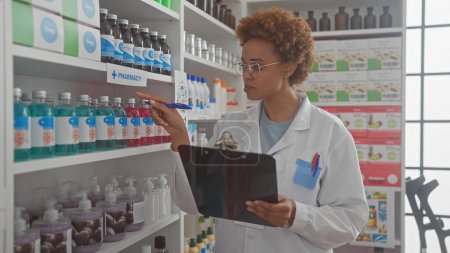 African woman pharmacist in white coat examining products with clipboard in a modern pharmacy.