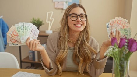 A smiling young woman in glasses holding singapore dollars indoors at home, portraying affluence and finance.