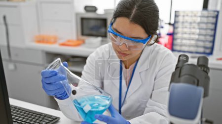Téléchargez les photos : Une scientifique hispanique mène une expérience en laboratoire, portant des lunettes de sécurité. - en image libre de droit