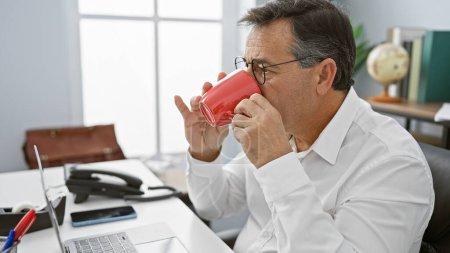 Téléchargez les photos : Homme d'affaires mature buvant du café dans un cadre de bureau moderne, exsudant un sentiment de professionnalisme et de confiance. - en image libre de droit