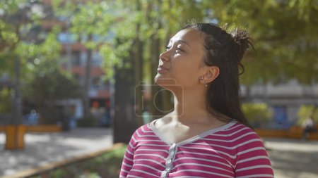 Photo for A contemplative young hispanic woman enjoys a serene moment outdoors in a lush city park. - Royalty Free Image