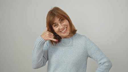 Mujer de mediana edad sonriente en un suéter azul haciendo un gesto de llamada sobre un fondo blanco