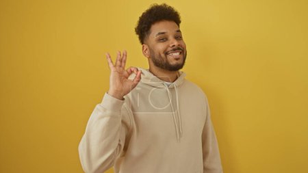 Téléchargez les photos : Souriant homme afro-américain donnant un geste correct isolé sur un fond jaune - en image libre de droit
