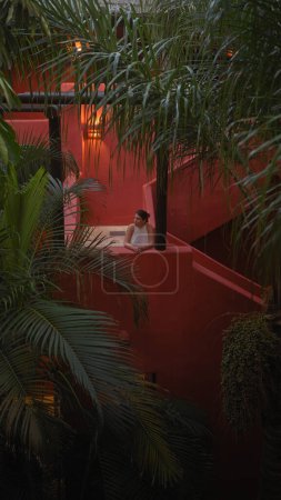 Foto de Una mujer serena se relaja en medio de una exuberante vegetación en un resort balinés tropical, que encarna tranquilidad y encanto exótico. - Imagen libre de derechos