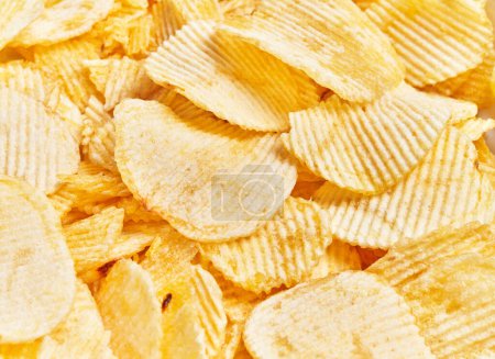 Close-up view of crispy, salty potato chips texture, implying a concept of snack, junk food, or comfort eating.