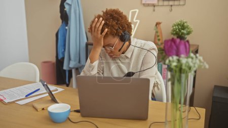 Foto de Mujer afroamericana estresada con auriculares trabajando remotamente en una oficina en casa. - Imagen libre de derechos