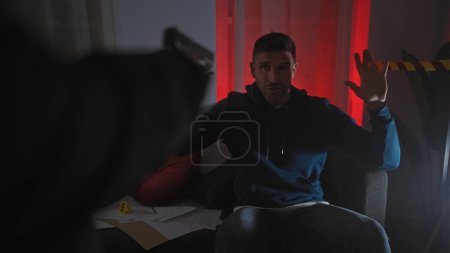 Photo for An officer aiming a gun at a man with raised hands in a dimly-lit room with red curtains and evidence markers. - Royalty Free Image