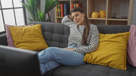 Téléchargez les photos : Jeune femme hispanique se détendre sur un canapé dans un confortable appartement salon. - en image libre de droit