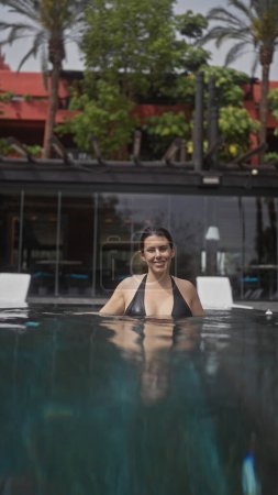 Foto de Mujer hispana joven disfrutando de un relajado baño en una piscina al aire libre en un bali resort, con ambiente tropical. - Imagen libre de derechos