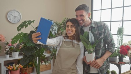 Un hombre y una mujer trabajadores floristas tomando una selfie juntos en el interior de una floristería llena de plantas.