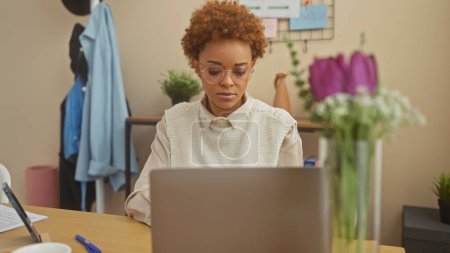 Téléchargez les photos : Femme afro-américaine professionnelle travaille sur ordinateur portable dans un cadre confortable de bureau à domicile. - en image libre de droit