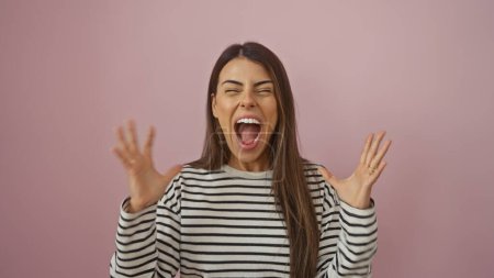 Foto de Mujer hispana gritando aislada contra un fondo de pared rosa, retratando emoción y emoción. - Imagen libre de derechos