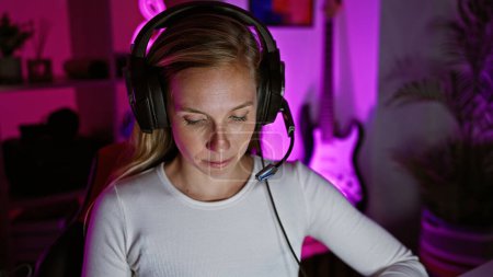 Foto de Una joven caucásica enfocada que usa auriculares en una sala de juegos oscura por la noche - Imagen libre de derechos