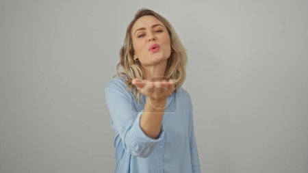 Photo for A young caucasian woman in a blue shirt blows a kiss against a white isolated background. - Royalty Free Image