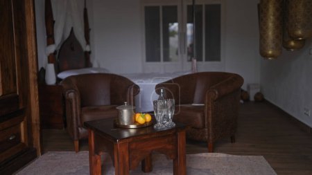 Téléchargez les photos : Élégant intérieur avec fauteuils en cuir, meubles en bois, lanternes décoratives et plateau avec théière et fruits - en image libre de droit