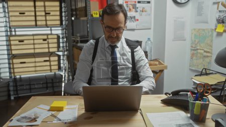 Téléchargez les photos : Homme barbu mature travaillant sur ordinateur portable dans le bureau de détective avec carte et documents. - en image libre de droit