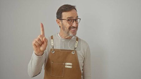 Photo for Smiling bearded mature man in apron gesturing against white background, portraying casual expertise. - Royalty Free Image