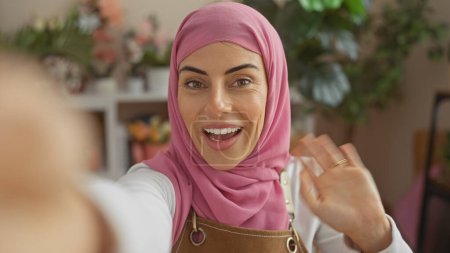 Foto de Una joven hispana sonriente en un hiyab rosa haciendo una videollamada en casa - Imagen libre de derechos